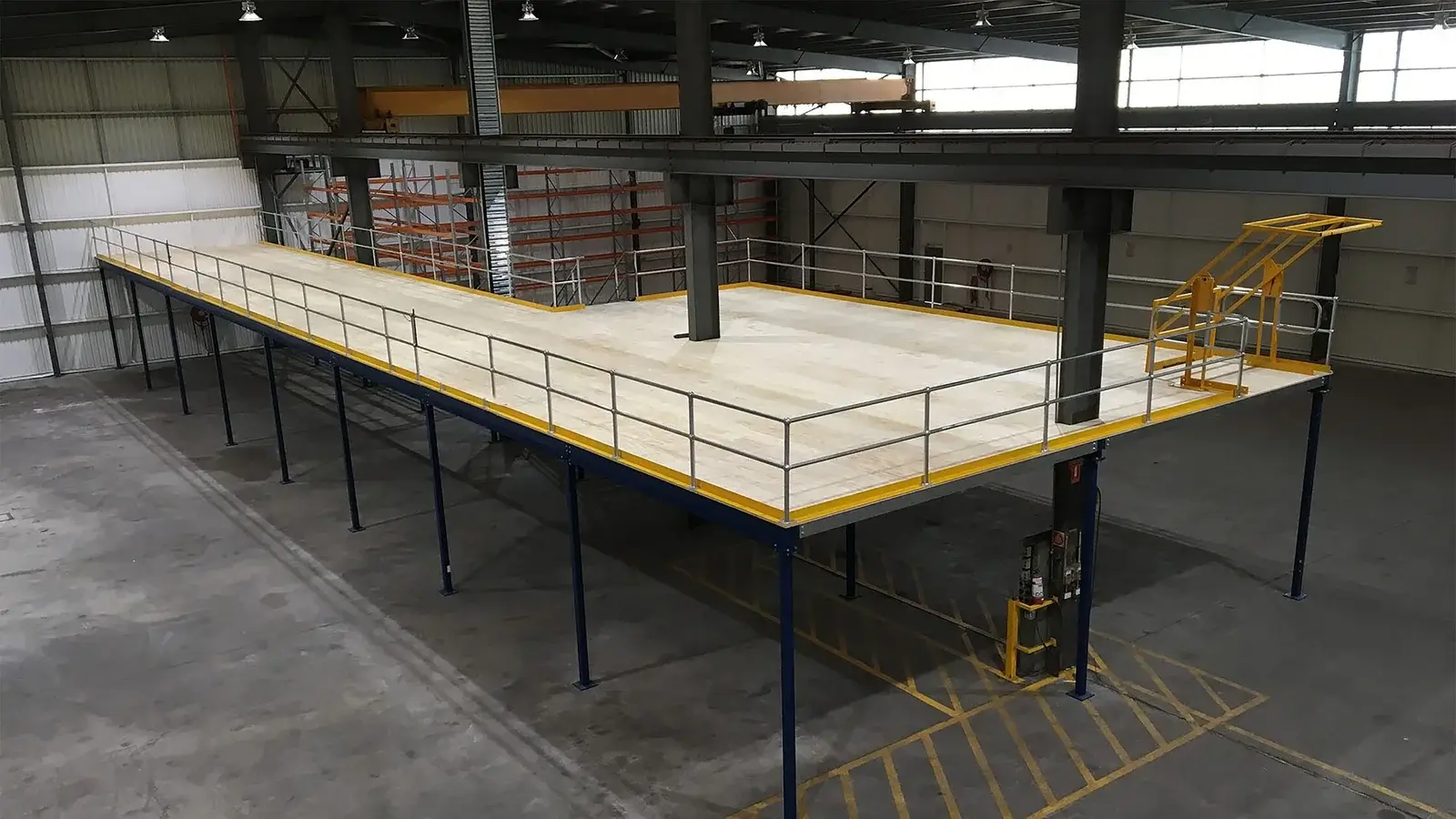 Industrial mezzanine floor structure inside a warehouse with steel columns, safety railings and access staircase.